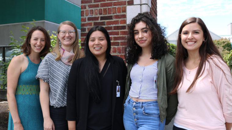 Five interns smile outside of a brick building.