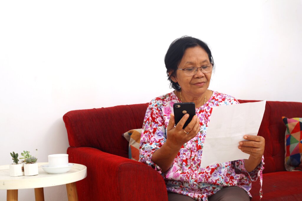 an elderly woman holds a smartphone and a piece of paper